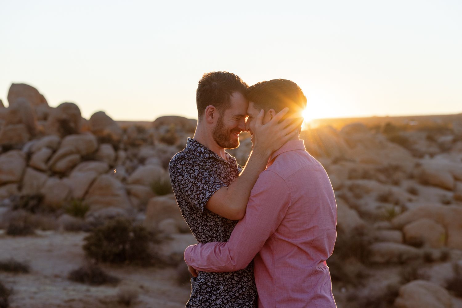 Silhouetted figures share intimate moment against warm sunset sky in desert landscape.