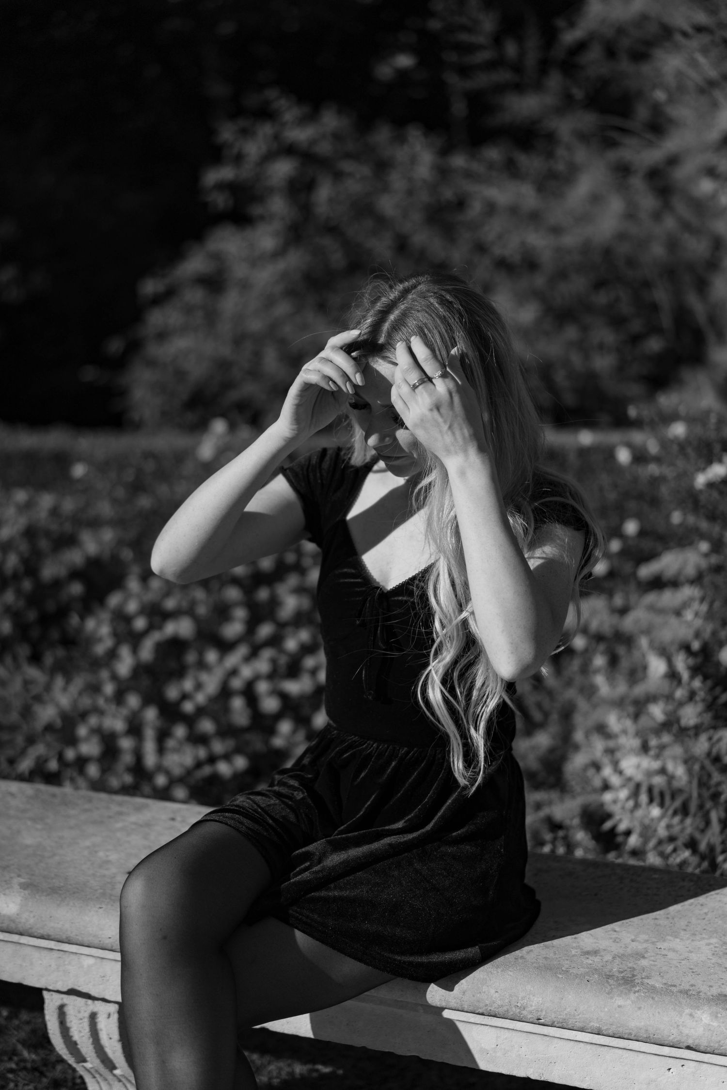 A black and white portrait of someone in a velvet dress sitting outdoors.