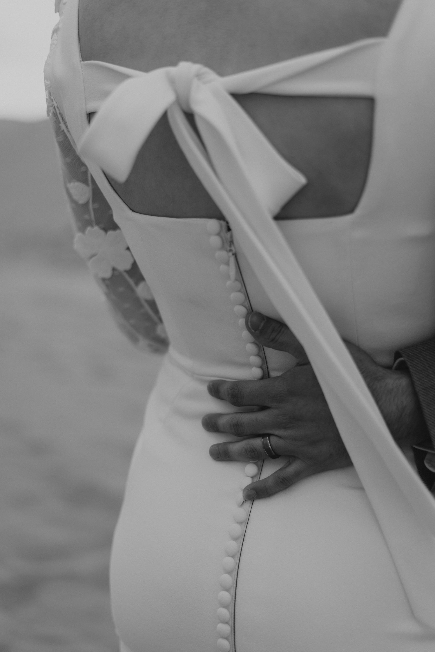 Close-up detail of a white wedding dress showing buttons and bow on the back.
