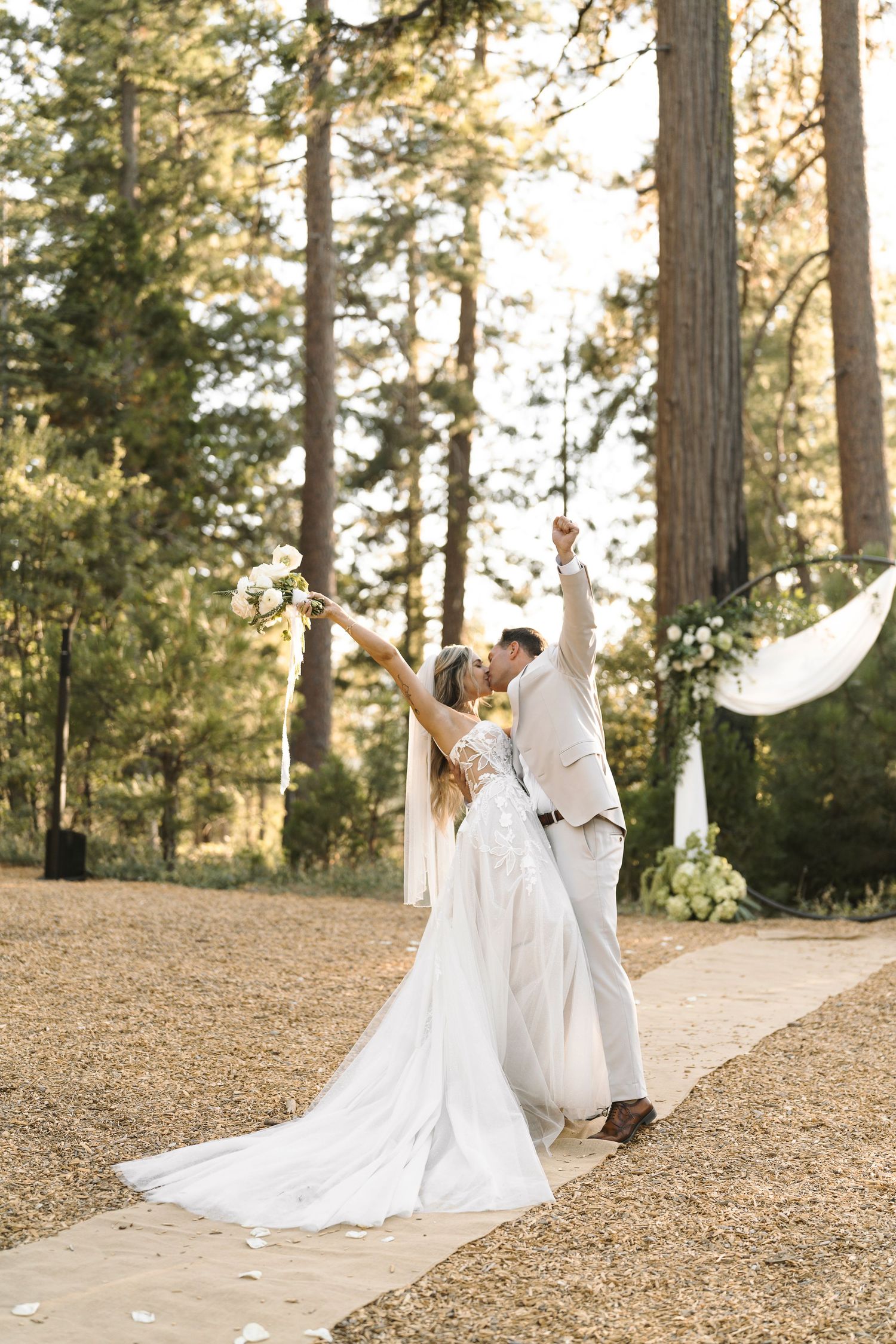 Couple dancing together on a hilltop surrounded by tall pine trees at sunset.