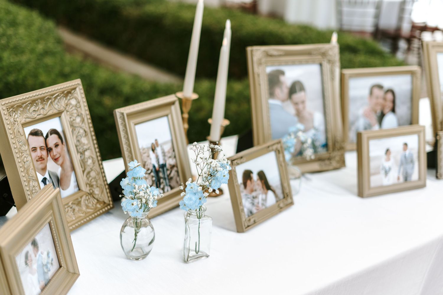 Wedding memories display with framed photos and blue flowers in delicate vases on white table.