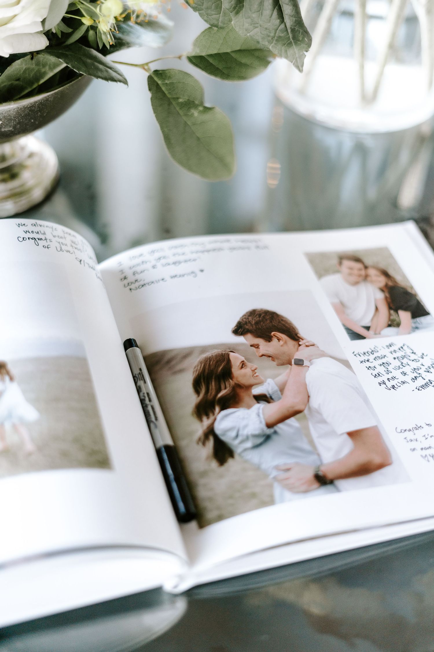 An open wedding guest book showing photos and handwritten messages beside white flowers.