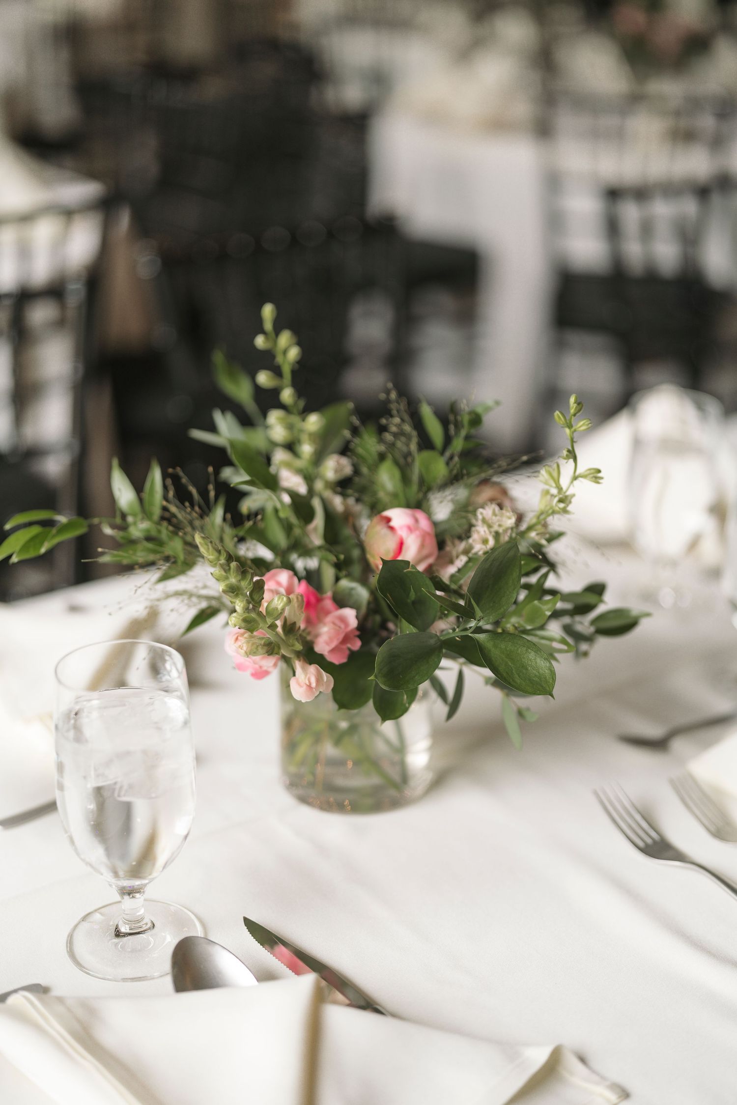 Elegant table setting with white linens, wine glasses, and delicate pink floral centerpieces in glass vases.
