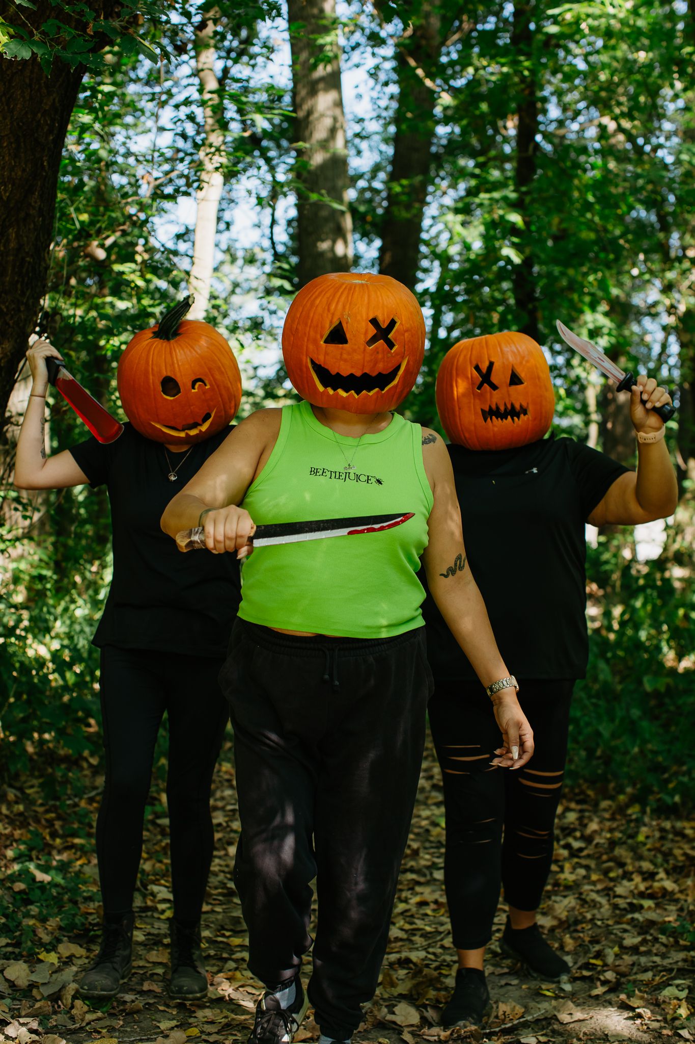 Row of people wearing pumpkin heads on their shoulders standing in a forest setting.