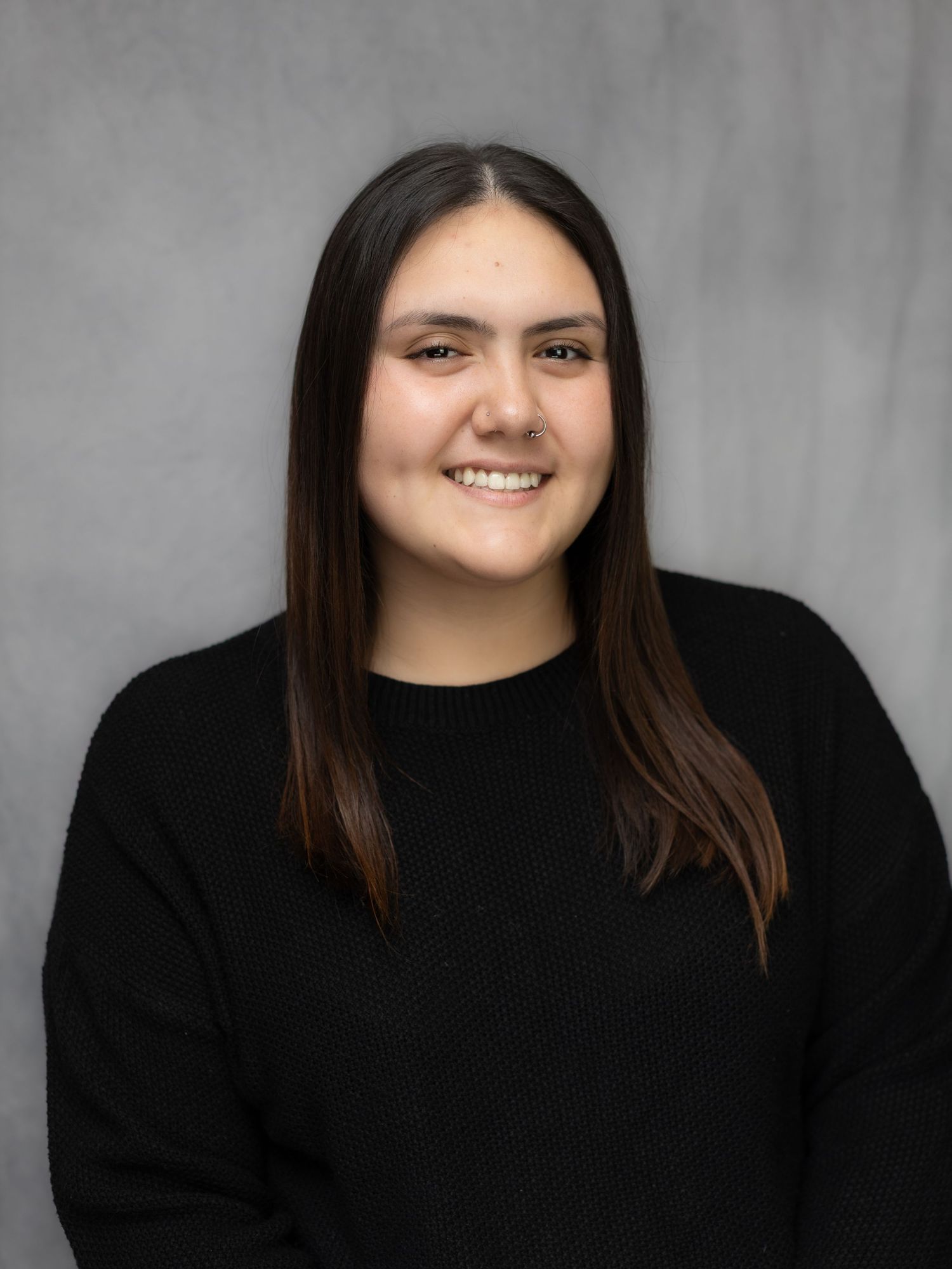 Portrait series against grey background wearing black sweater.
