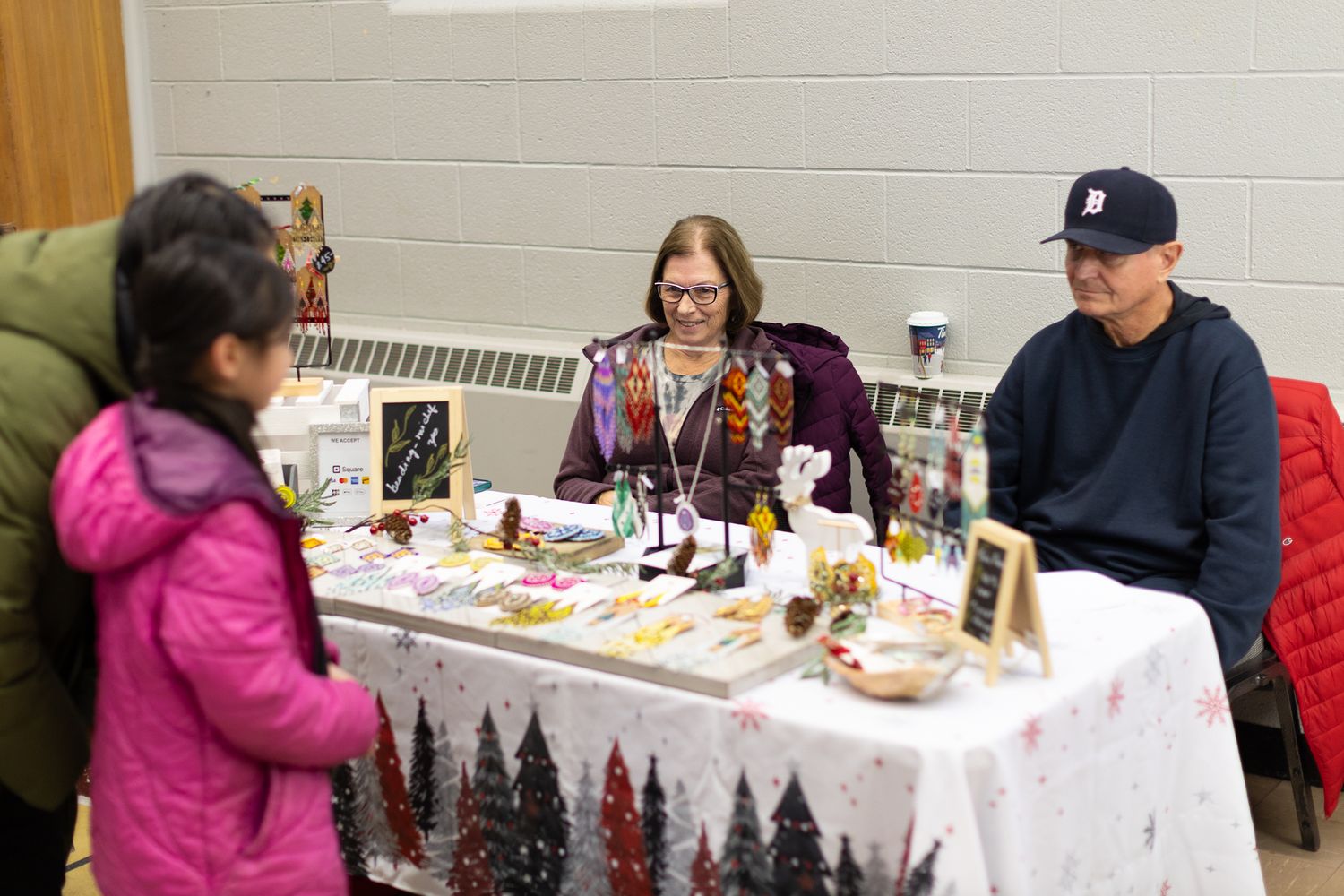 Craft fair vendors displaying merchandise on white-clothed tables in a community space.