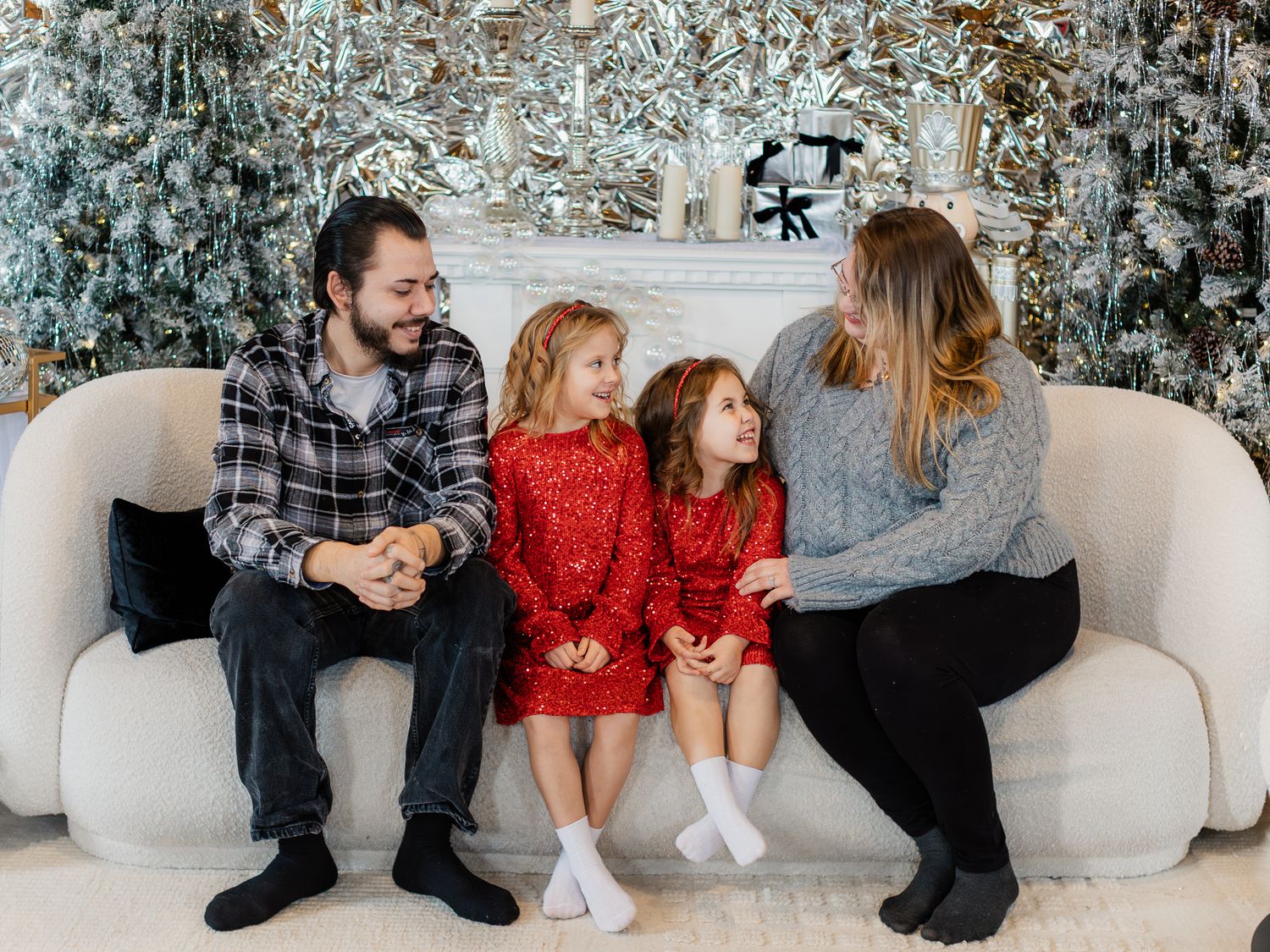 Family sitting together on white couch with frosted Christmas tree in background.