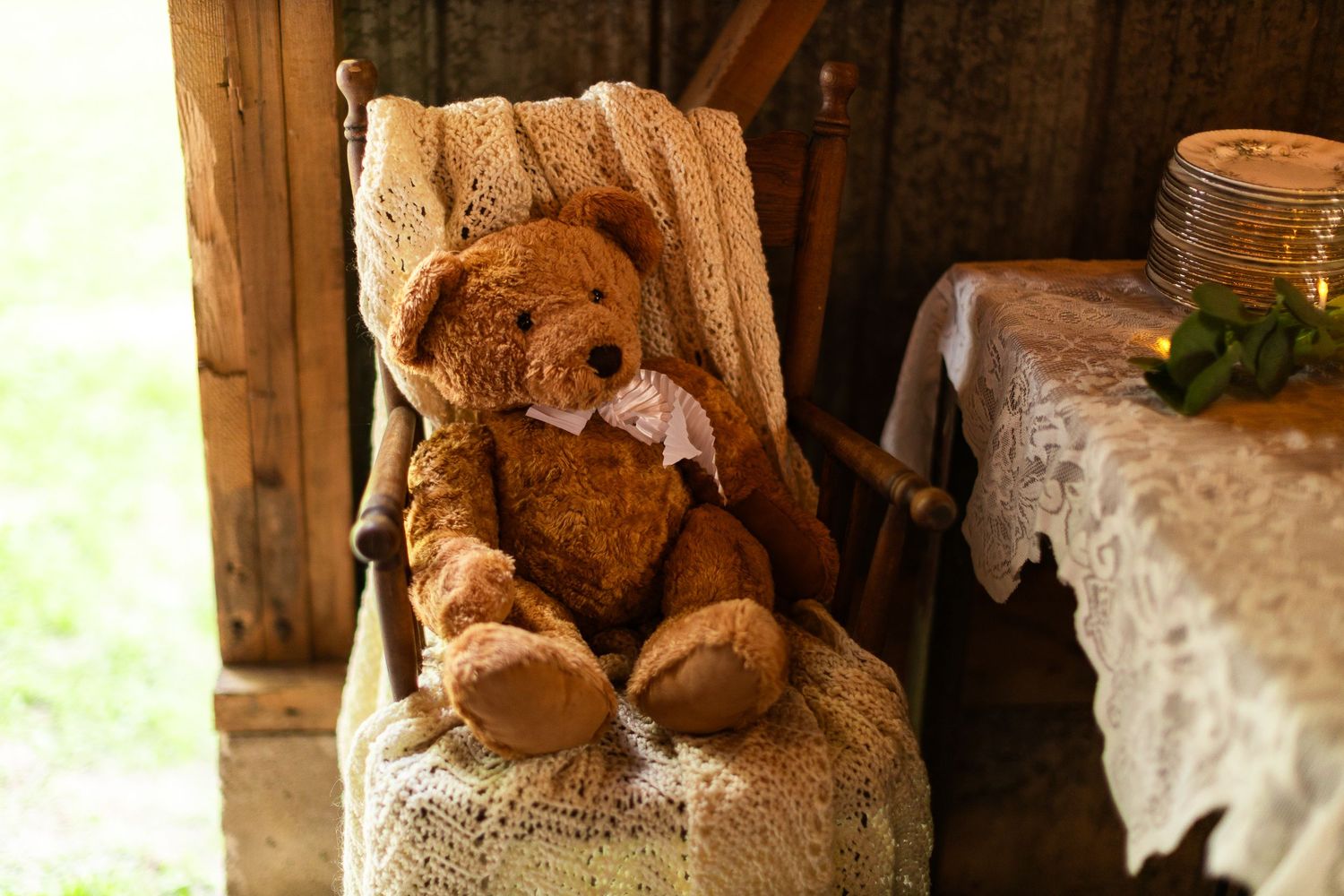 A brown teddy bear sitting in a vintage chair with lace decorations.