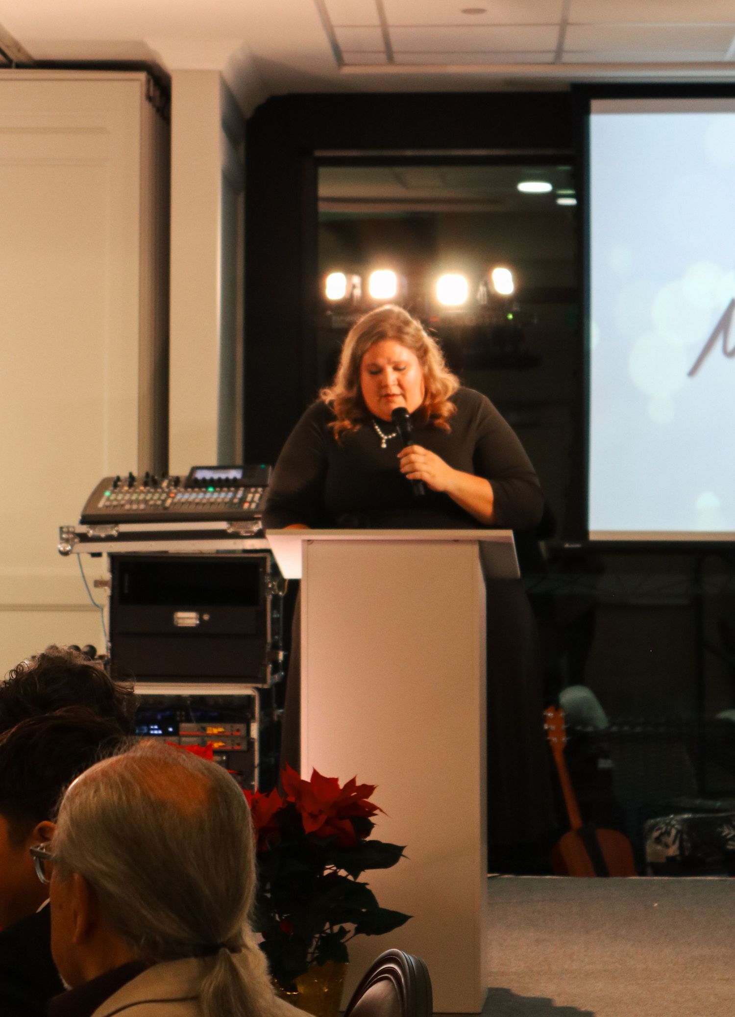 Dark event space with audiovisual equipment and scattered lighting visible in the background.