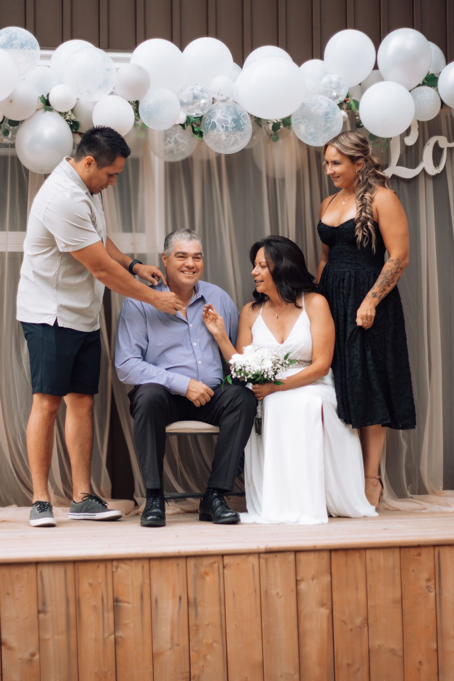 Wedding guests gather on a wooden deck decorated with white balloons for celebration photos.