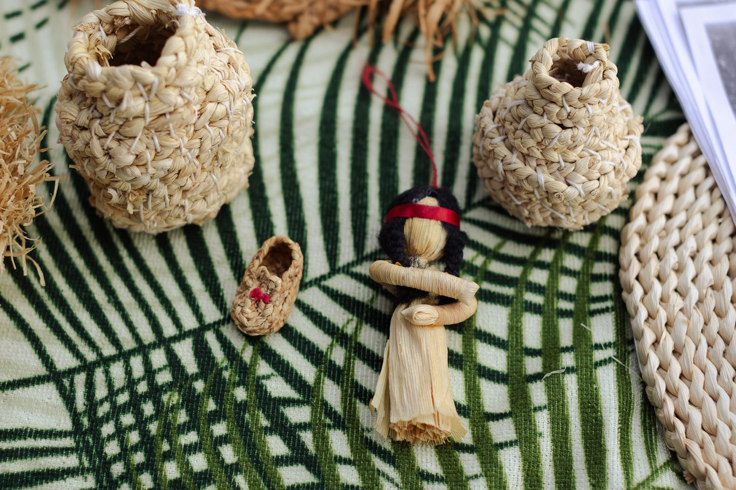 Handmade Indigenous crafts including woven baskets, a corn husk doll, and a small beaded shoe on a woven mat.