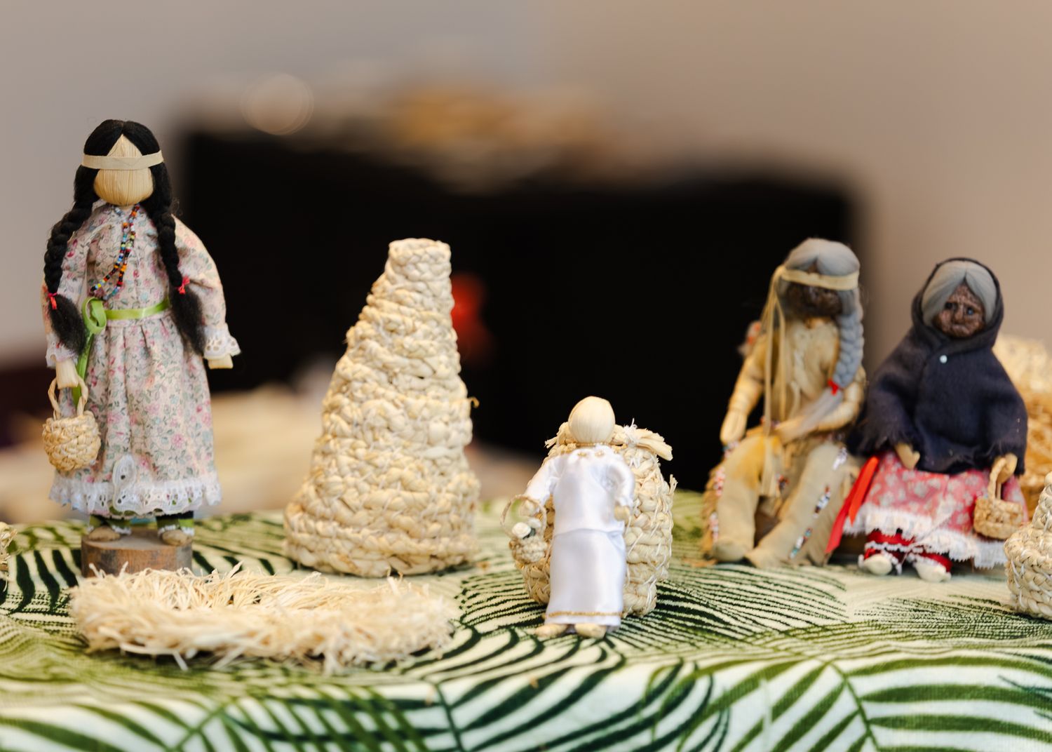 Traditional handcrafted Indigenous dolls and figurines displayed on a decorative fabric surface.