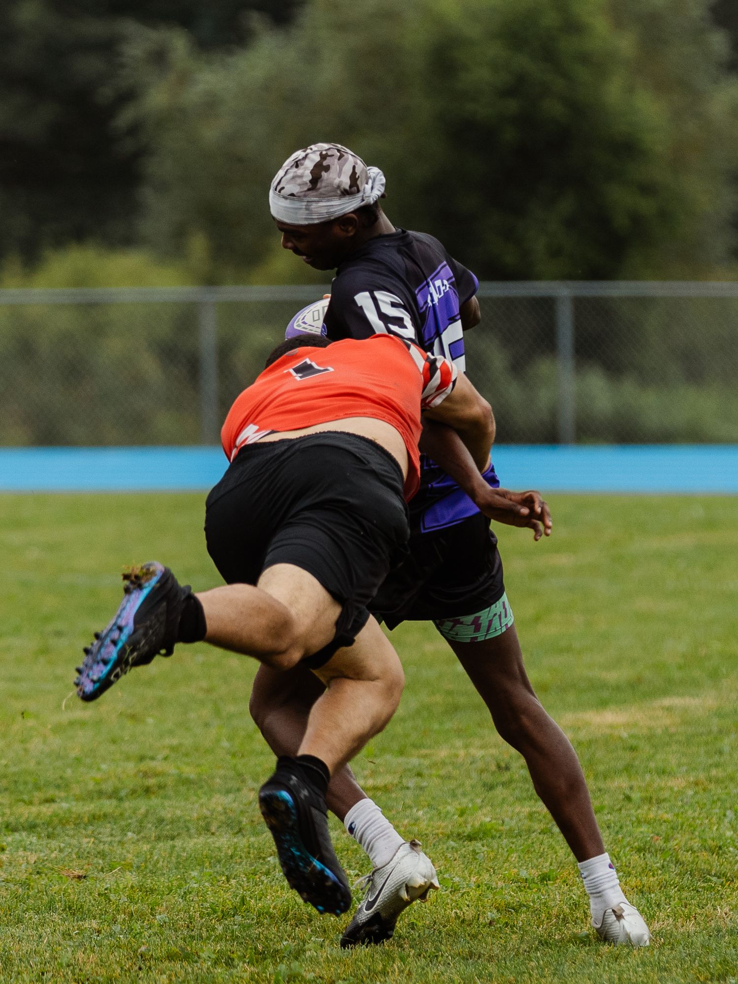 Two rugby players collide during an intense tackle on a green grass field.