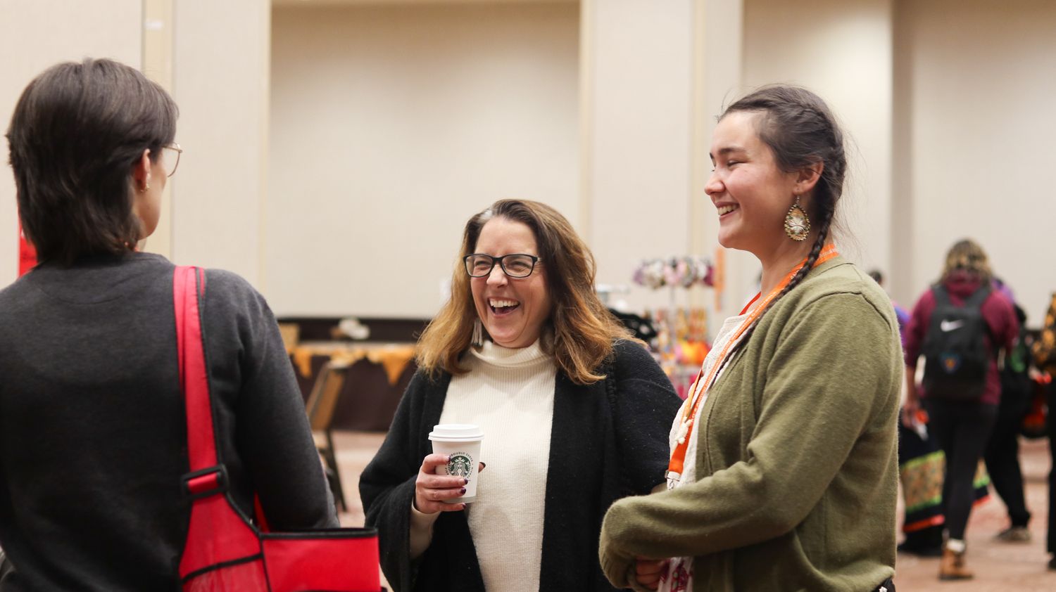 Three women laughing and conversing at an indoor networking event or conference gathering.