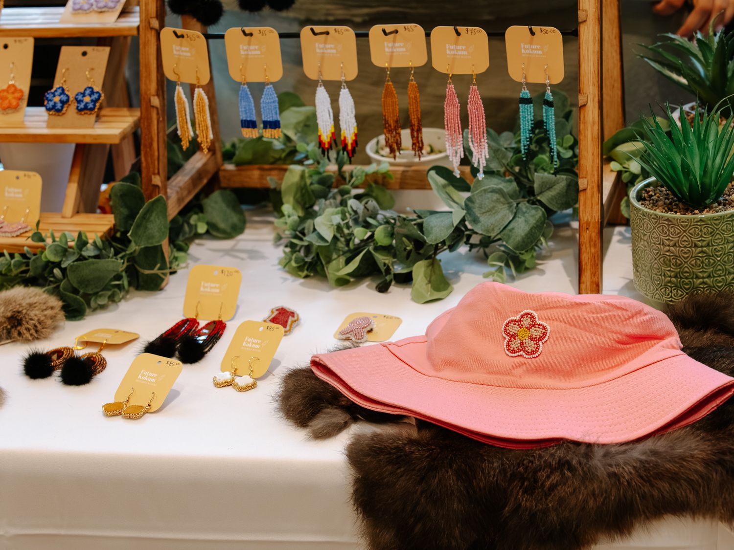 Handmade earrings, hair accessories, and pink floral bucket hat displayed on craft market table.