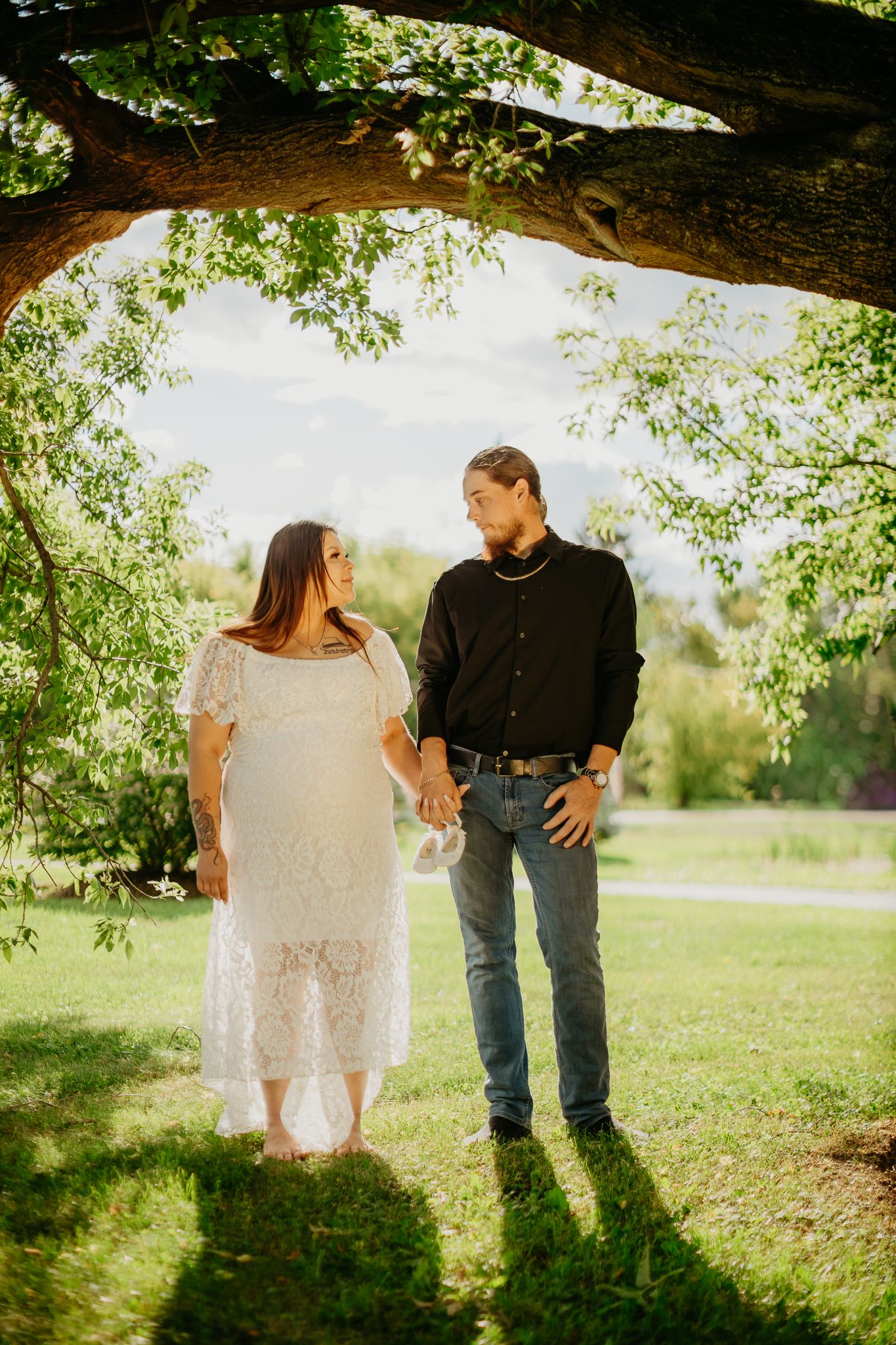 A couple shares a tender moment under a tree branch in a sunlit park setting.