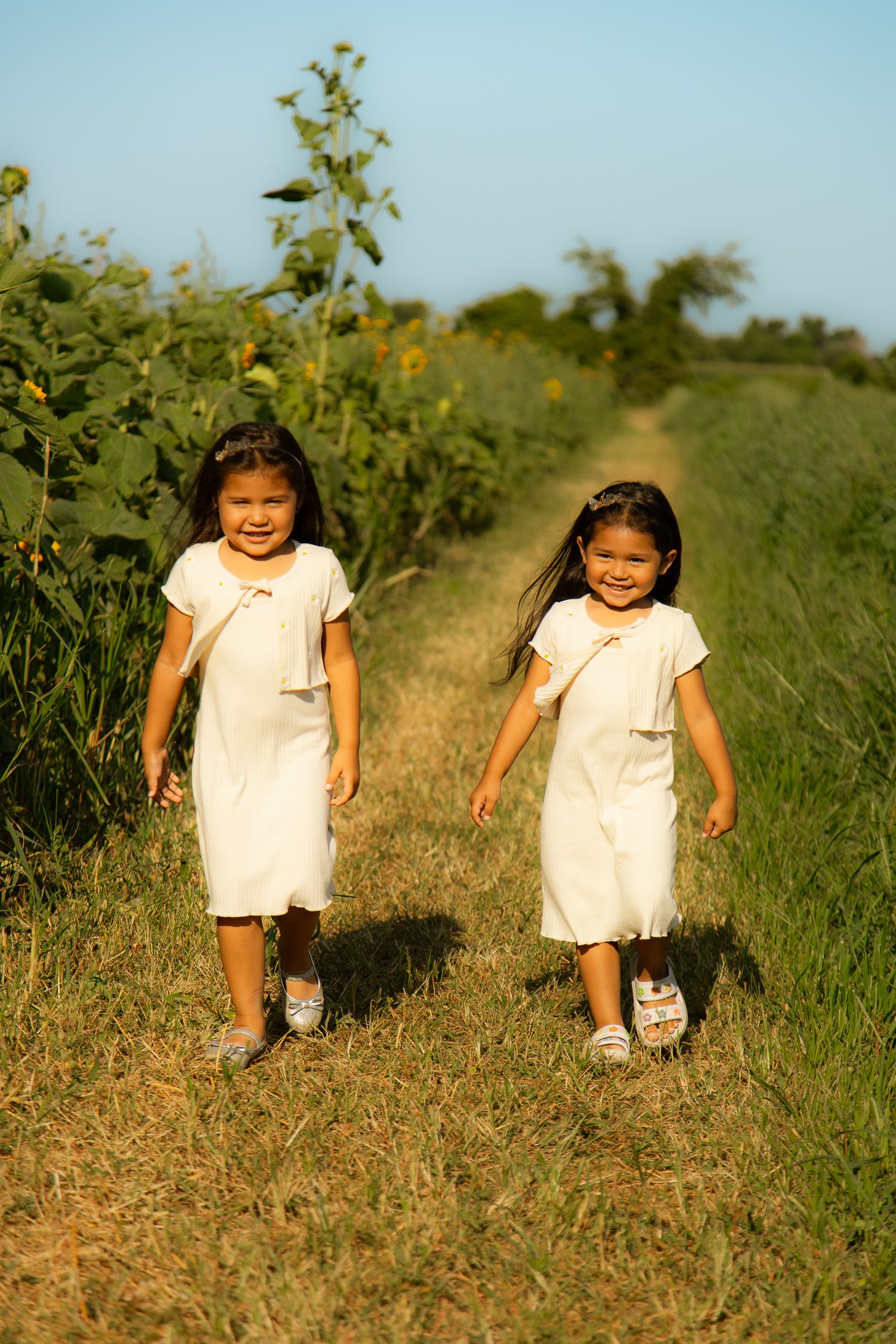 Children running along a dirt path through a field of wildflowers on a sunny day.