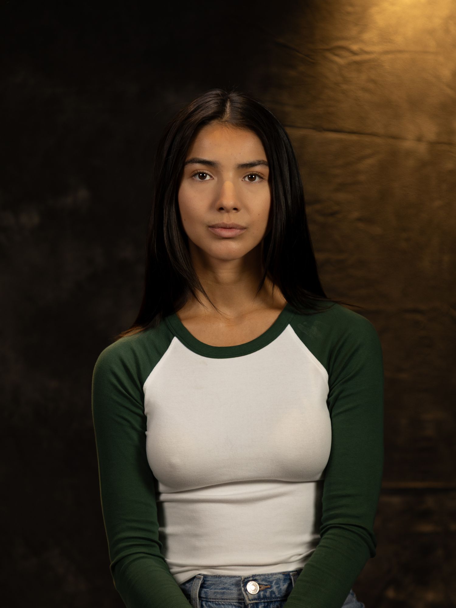 Studio portrait showing person in green and white baseball tee against textured backdrop.