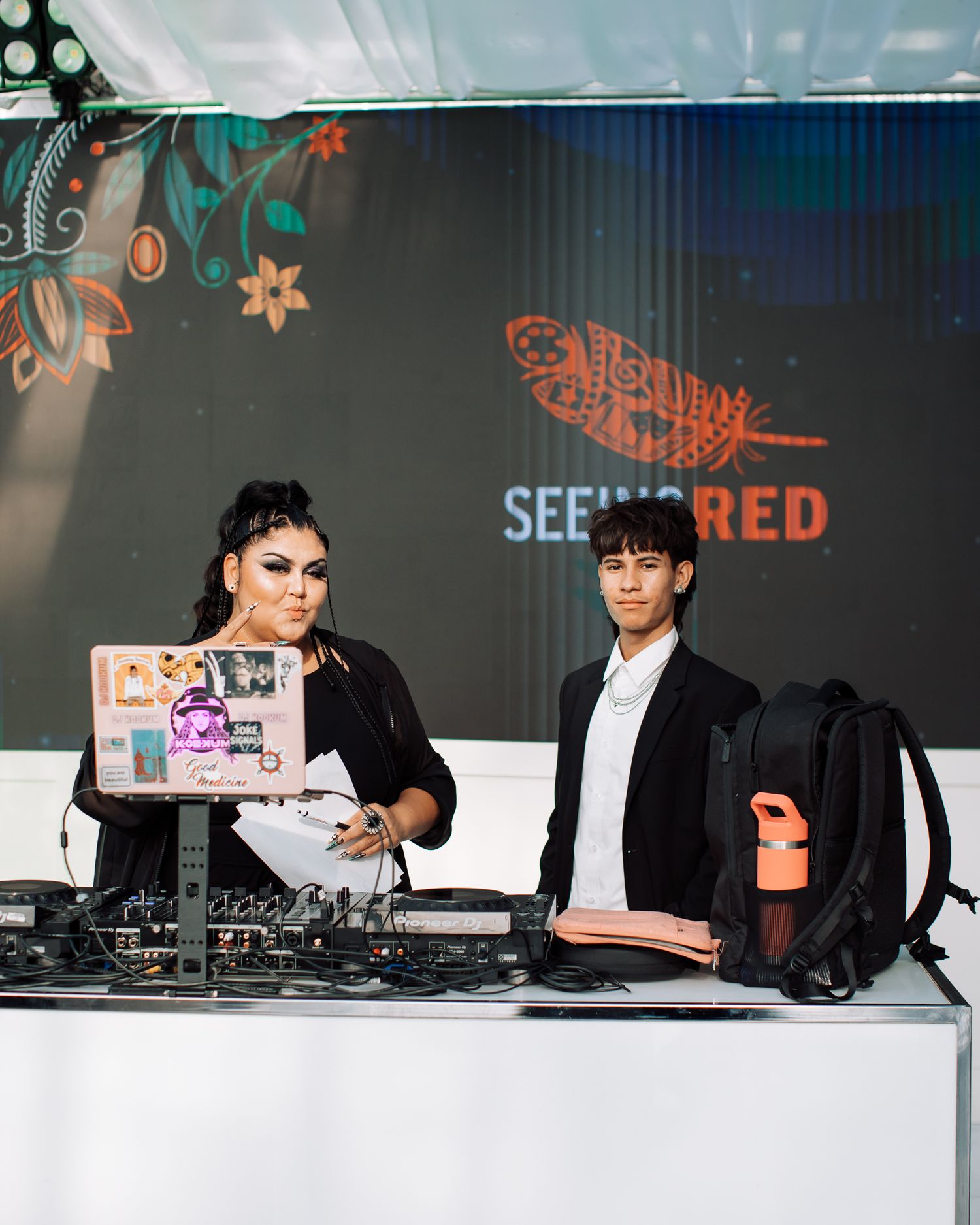 Two DJs at a Seeing Red event setup with DJ equipment and laptop in an outdoor venue.