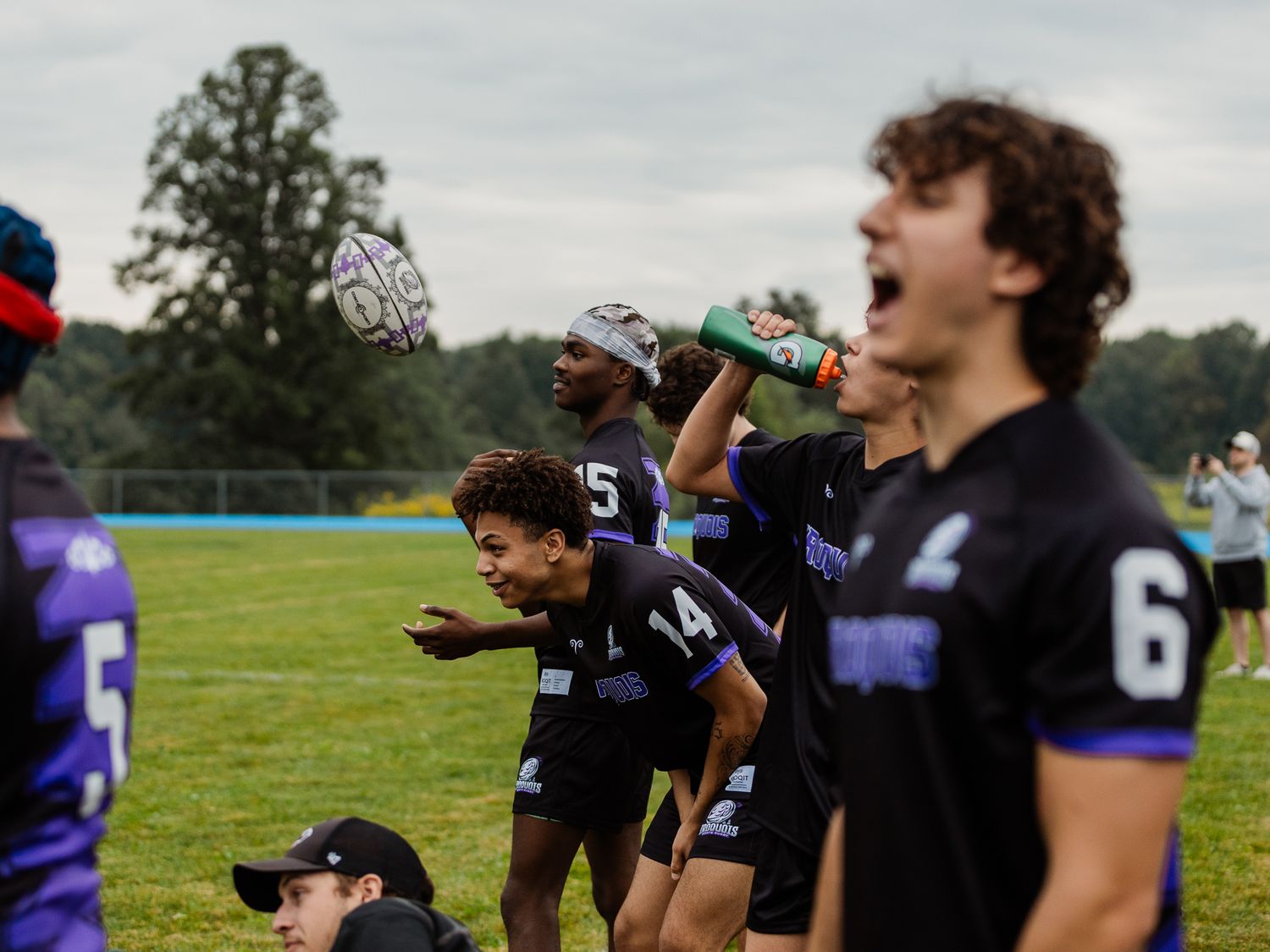 Youth ultimate frisbee players in black uniforms celebrate on a green field during a competitive outdoor tournament game.