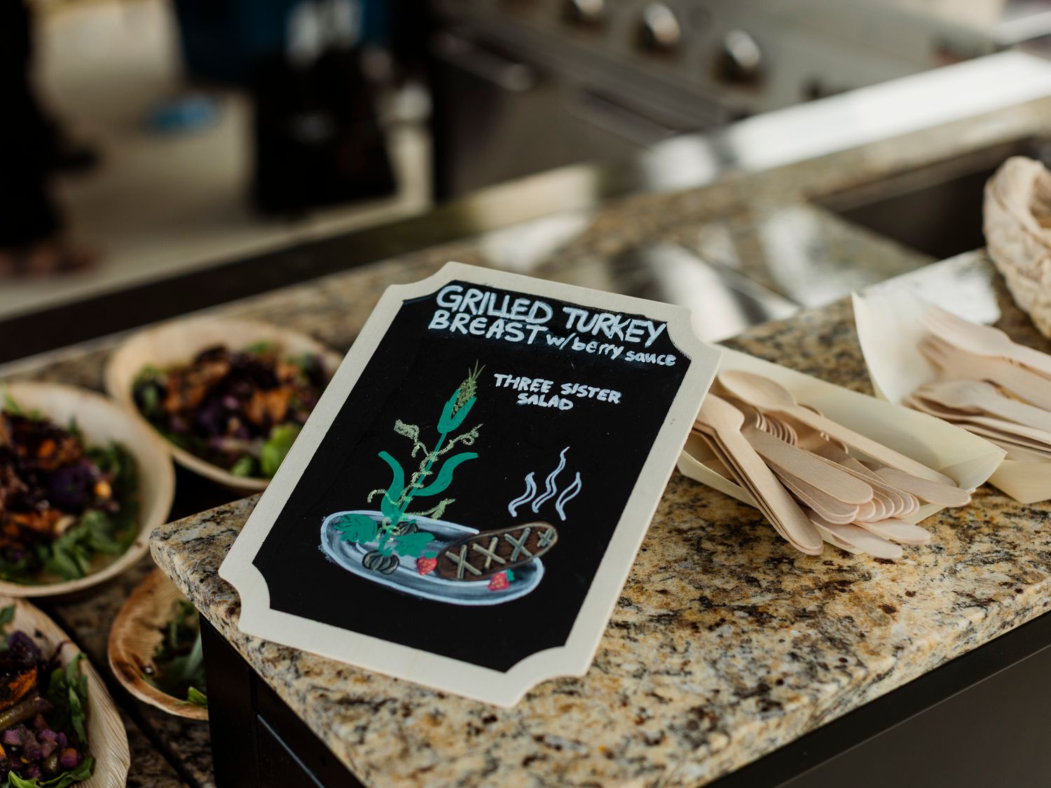 A chalkboard sign for grilled turkey breast three spiced salad displayed on a granite counter at a food station.