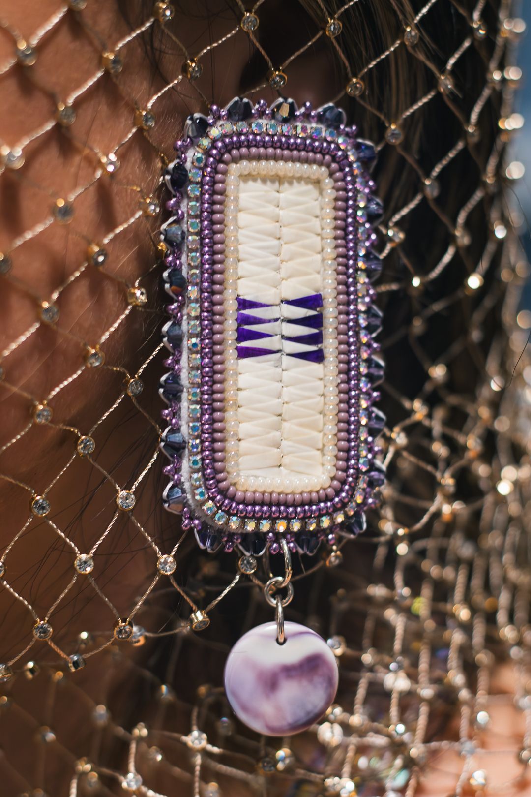 Handcrafted rectangular brooch with purple beading, white quillwork, and a lavender shell pendant on a beaded net backdrop.