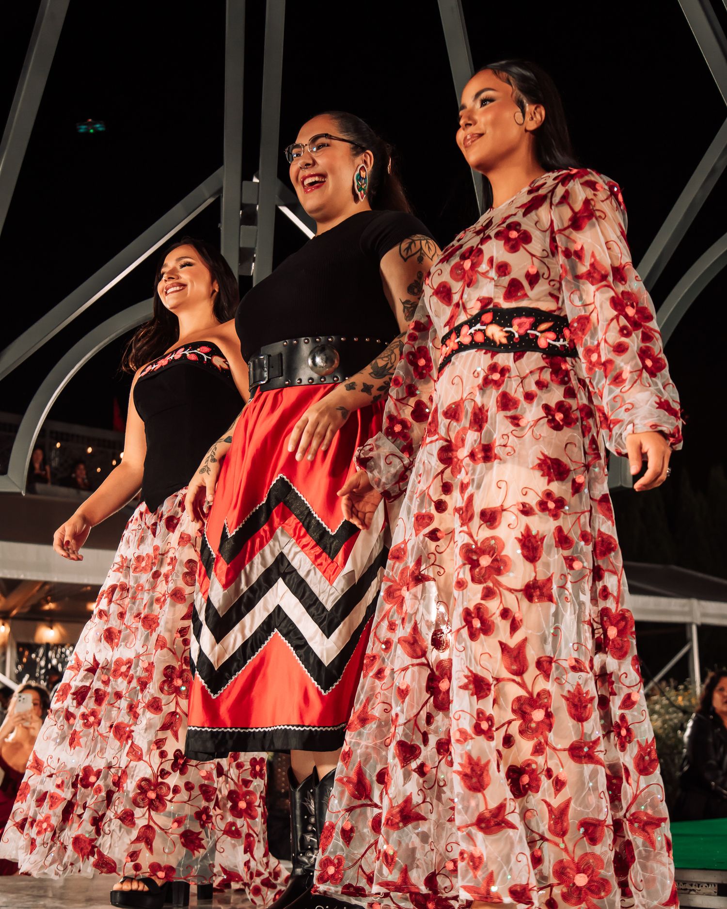 Models walk the runway wearing floral print dresses with geometric patterns during an evening fashion show.