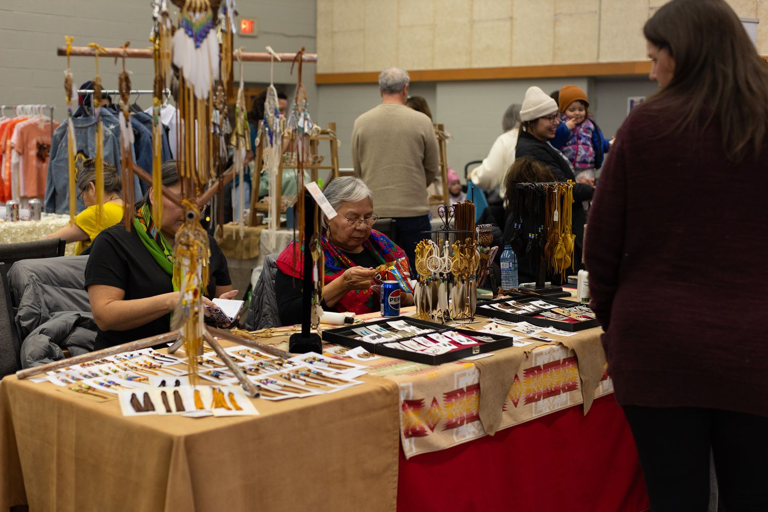 Handmade crafts and merchandise displayed on tables at an indoor artisan market.