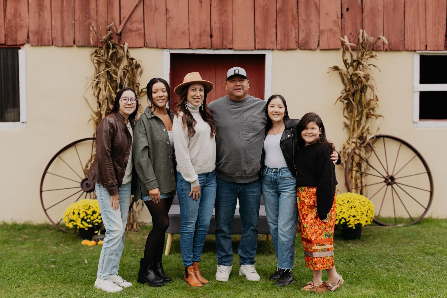 A large family group poses together in front of a rustic barn decorated for fall.