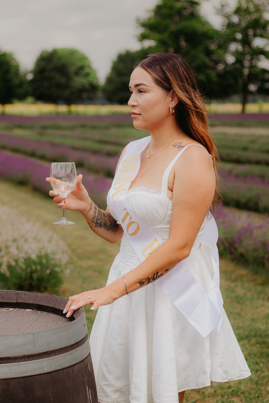 Woman in white sundress enjoying drinks in garden setting with lavender flowers.