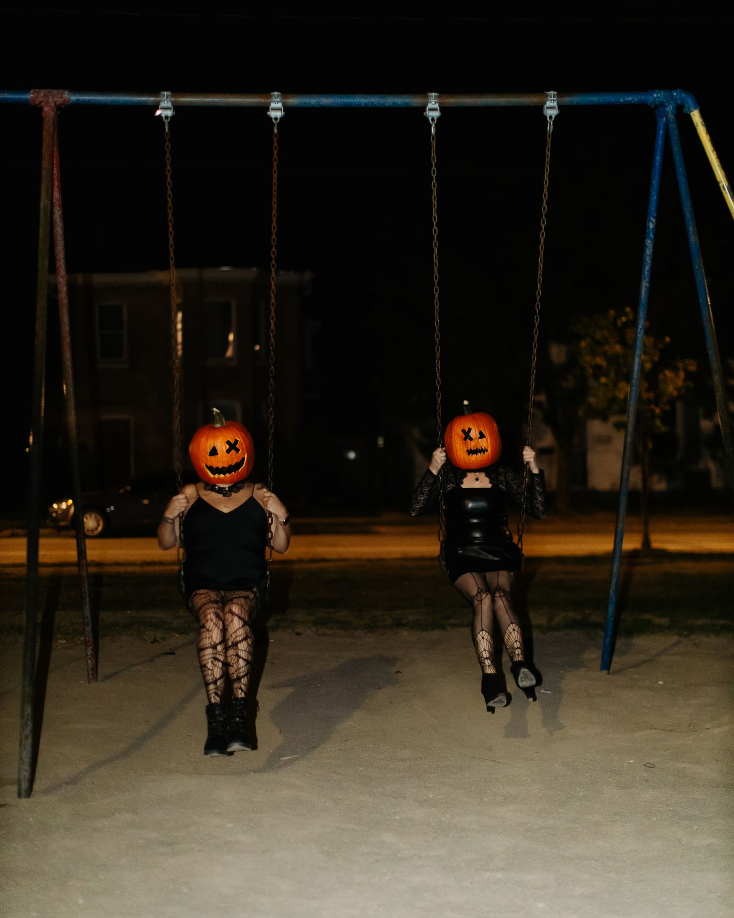 Figures with pumpkin heads sitting on playground swings at night.
