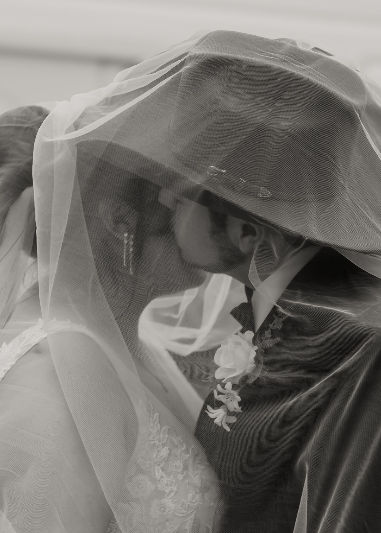Black and white photo of bride and groom kissing under wedding veil, groom wearing a cowboy hat.