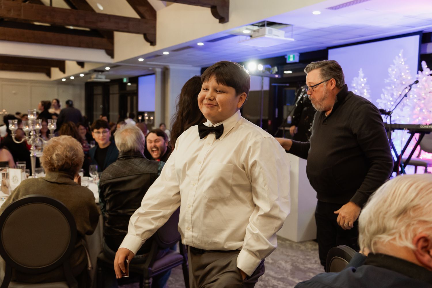 People gathered at an indoor event venue with purple lighting and holiday decorations.