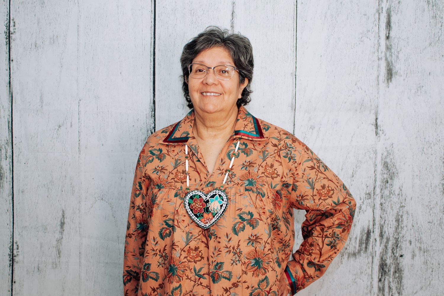 Person wearing a peach floral print top against a white wooden wall background.