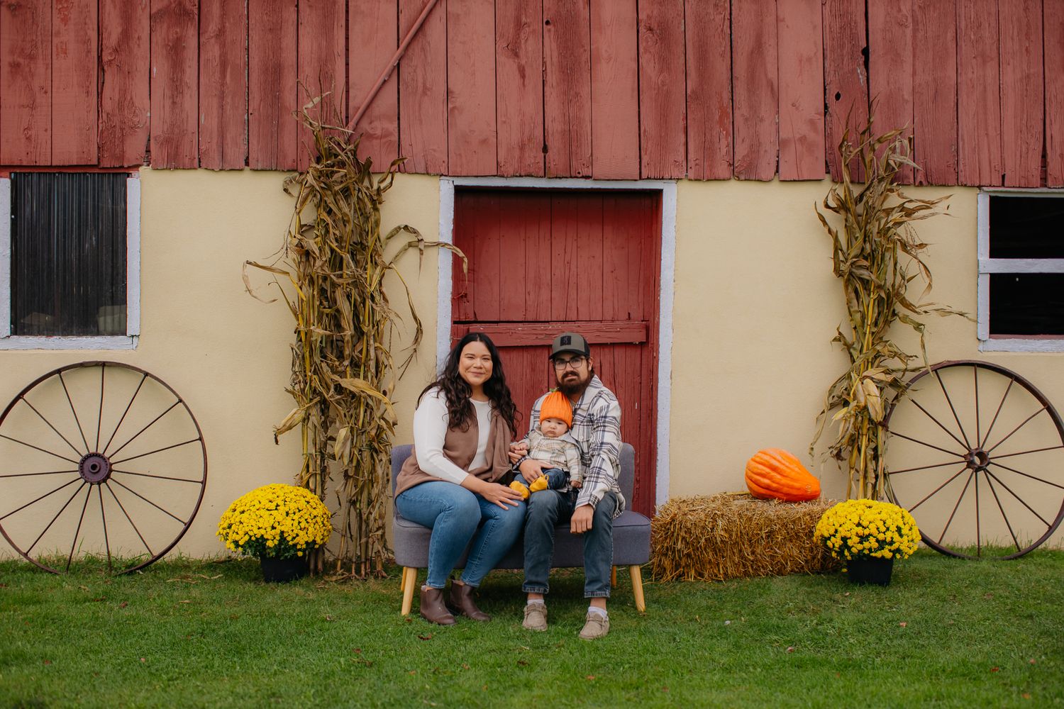 A casual family portrait session takes place outside a charming red barn with autumn decorations.
