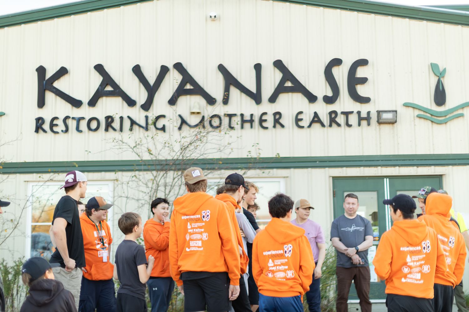 Row of orange-clad volunteers standing in front of a building with Kayanase signage.