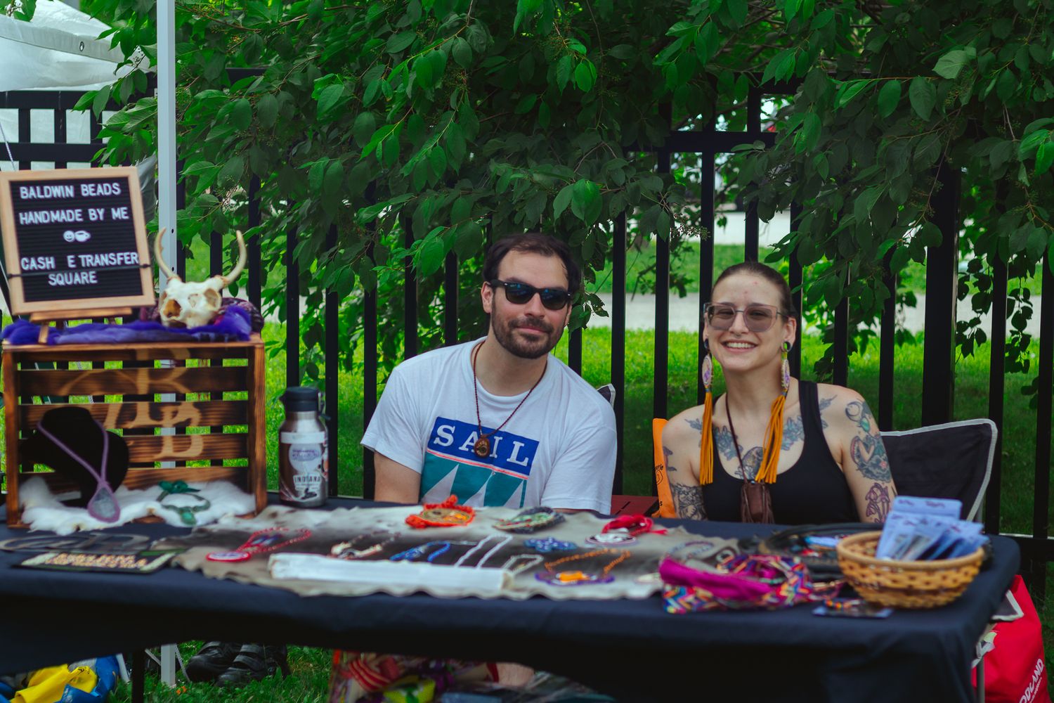 Vendor booths and attendees gathered at an outdoor cultural festival under tree canopy.