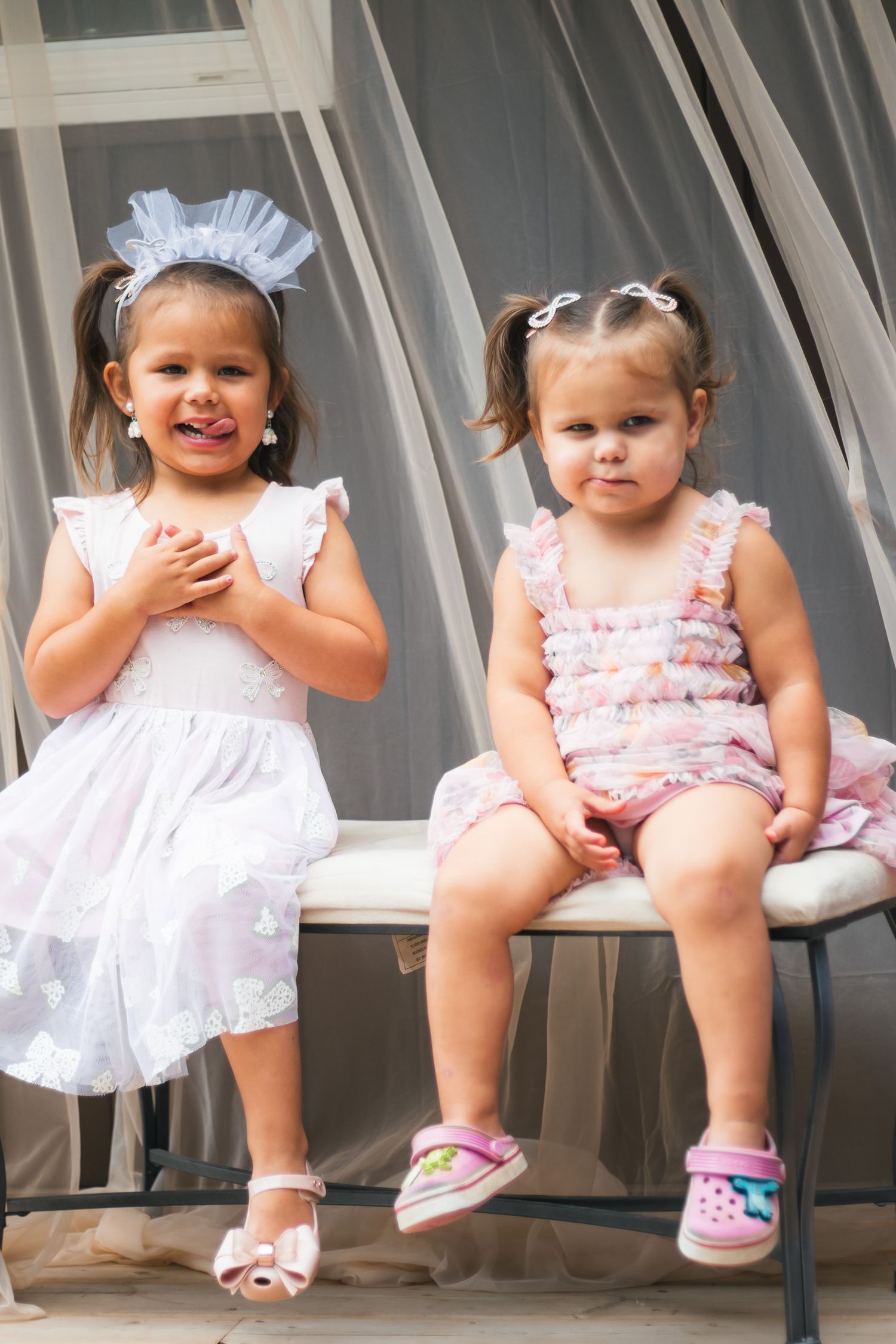 Two adorable little girls in white and pink dresses sitting together at a wedding.