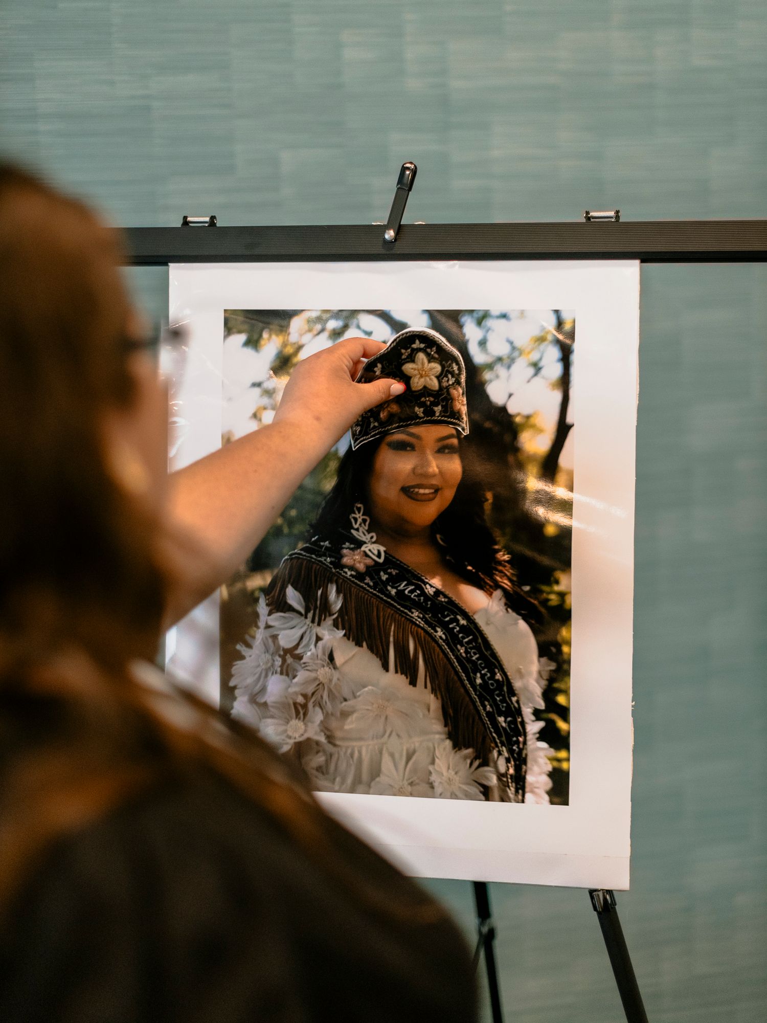 Person pointing at a framed photo of a woman wearing traditional Native American regalia and beaded crown on an easel.