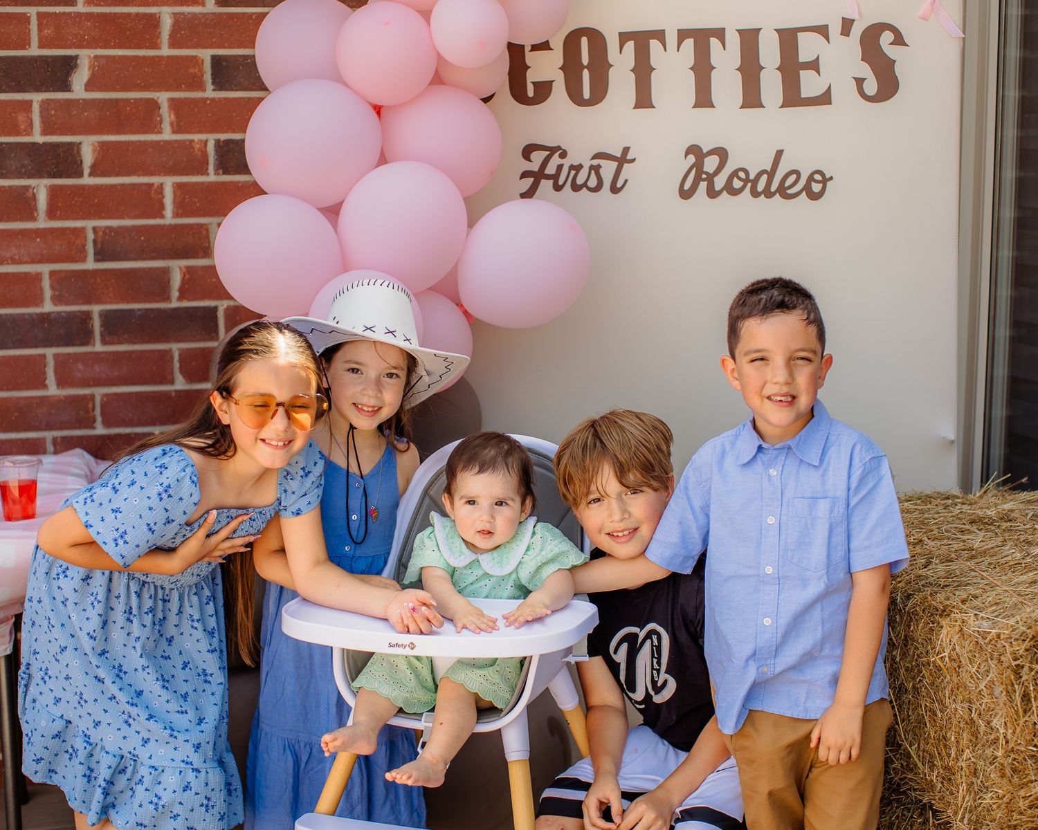 Five children pose at a cowboy-themed first birthday party with pink balloons and a Cottie's First Rodeo sign.