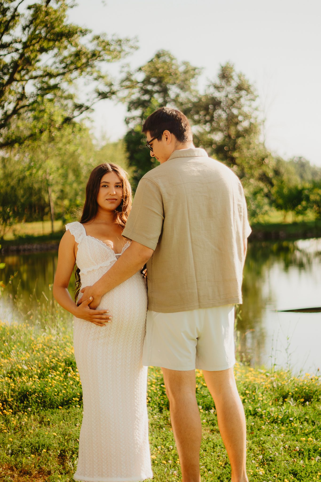 Expecting couple embracing by pond during golden hour photography session.