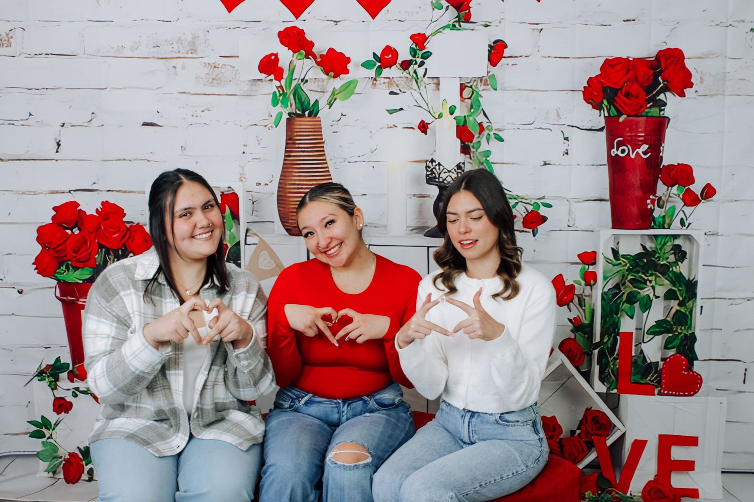 Group portrait against white brick wall with red hearts and valentine decorations.