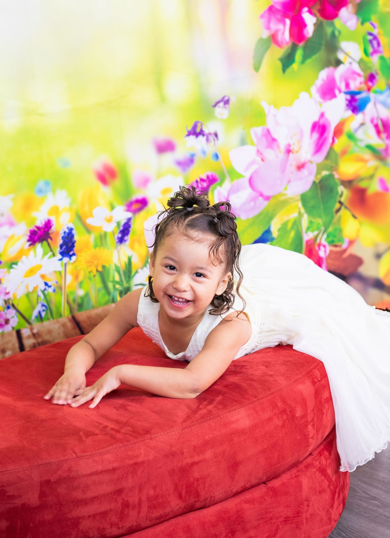 A joyful portrait on a red velvet couch with vibrant flowers in the background.