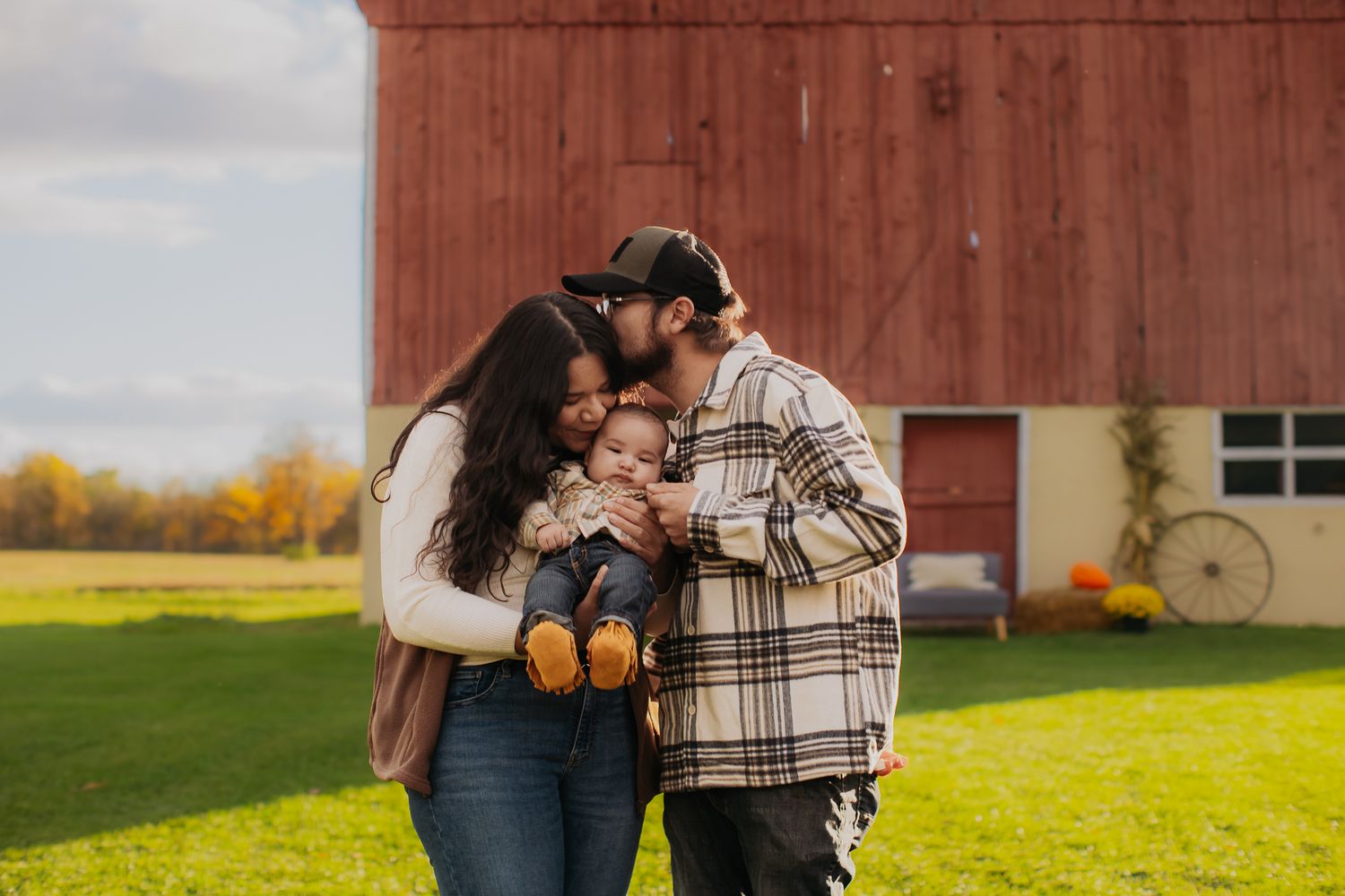 A family shares intimate moments during a fall photoshoot by a rustic red barn.