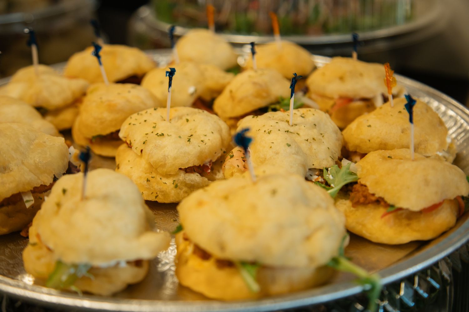 Close-up of mini sandwiches with toothpicks arranged on a silver serving platter.
