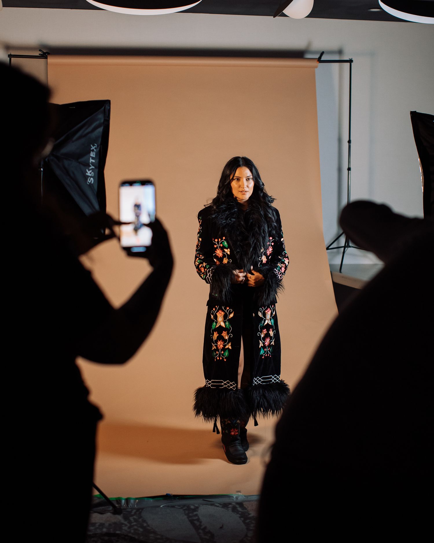 Behind the scenes photo shoot with fashion model against orange backdrop.