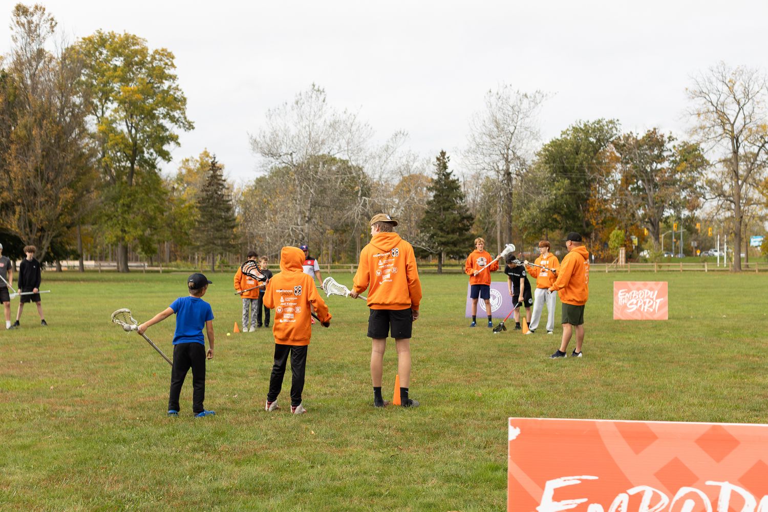 People in orange shirts spread out across an open field during autumn activities.