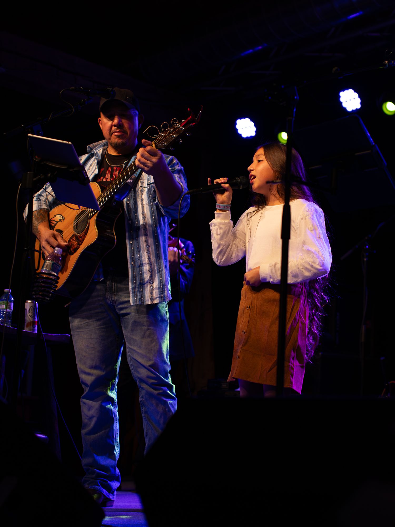 Musicians playing instruments on a dimly lit stage with blue accent lighting during a performance.
