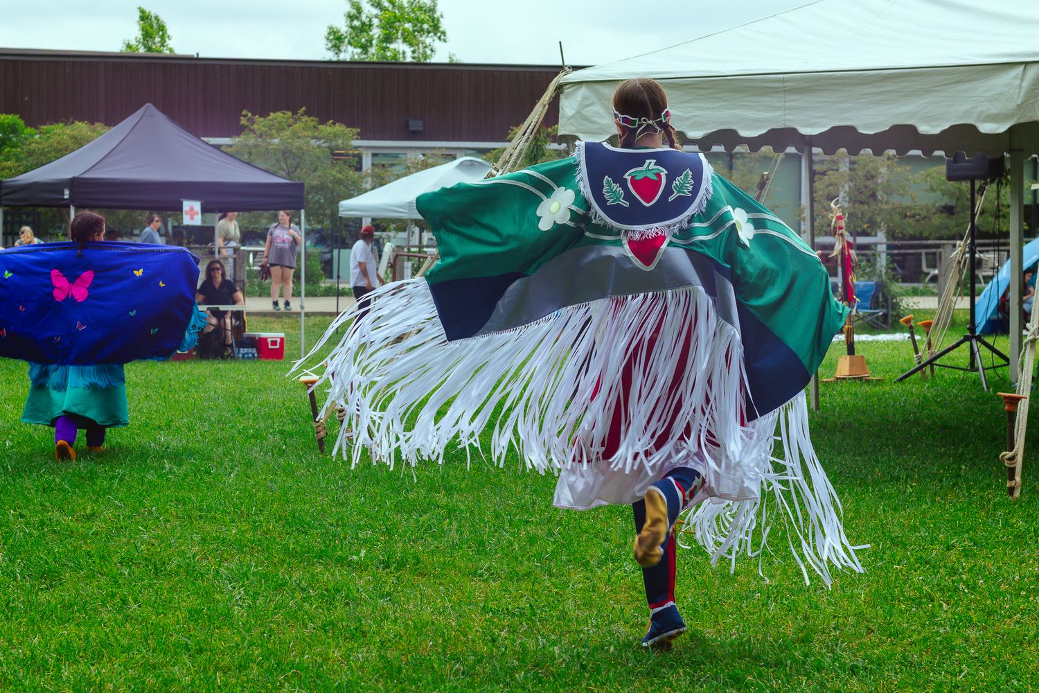 Traditional dancers performing in regalia with fringed outfits on grass.