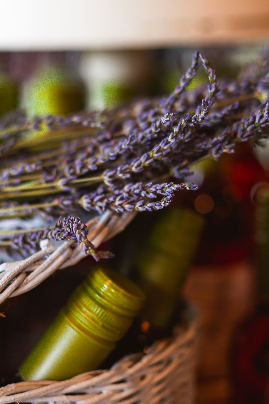 Dried lavender sprigs resting in a wicker basket with green wine bottles in soft bokeh background.